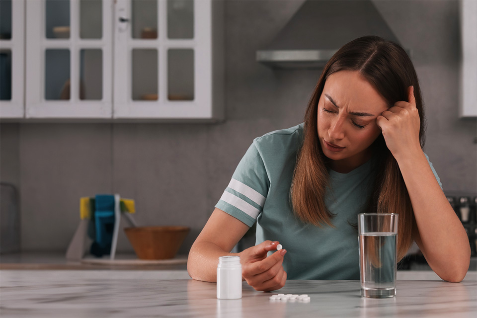 Depressed woman with glass of water and antidepressant pills at table in kitchen